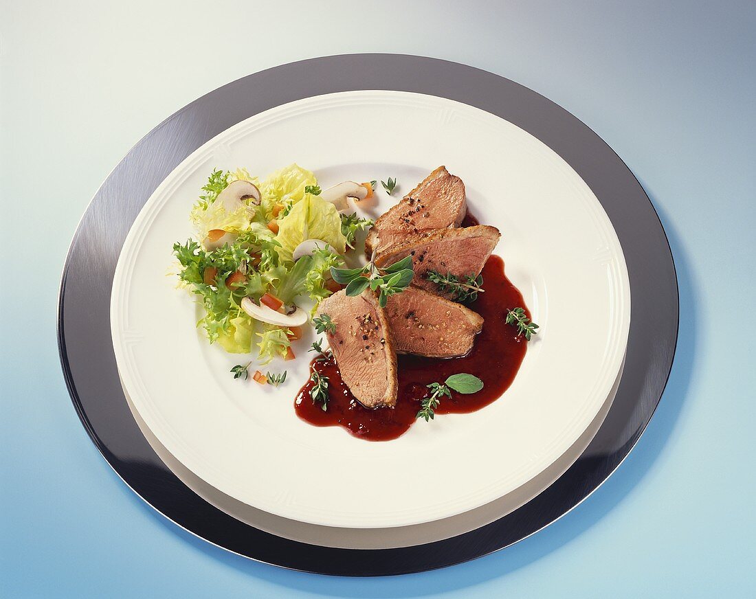 Slices of duck breast with sauce & salad garnish on plate