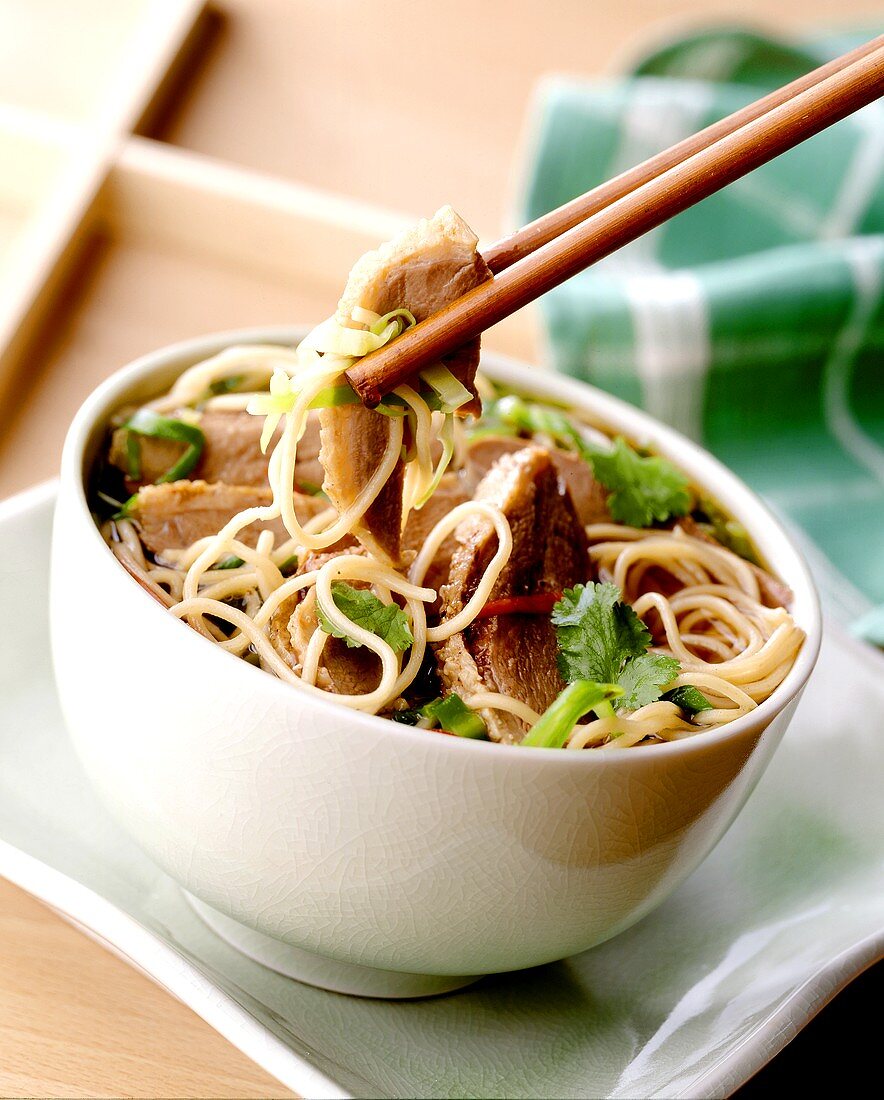 Duck on noodles with coriander leaves in bowl & on chopsticks