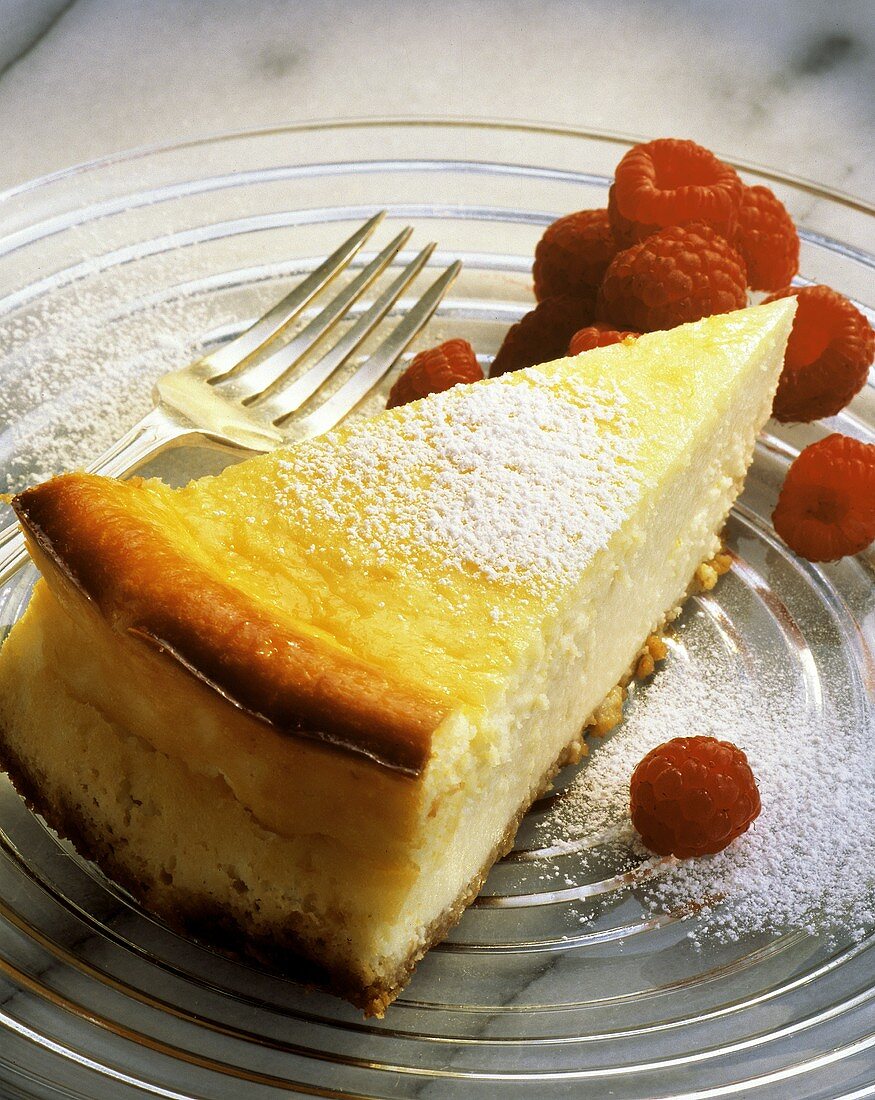 A piece of lemon cheesecake with icing sugar & raspberries