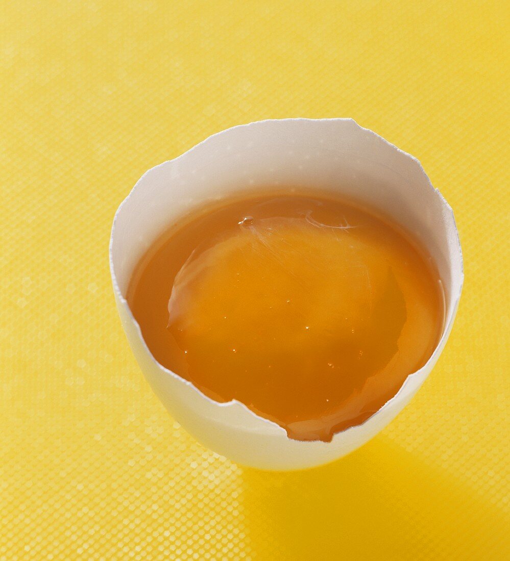 Egg yolk in half egg shell on yellow background