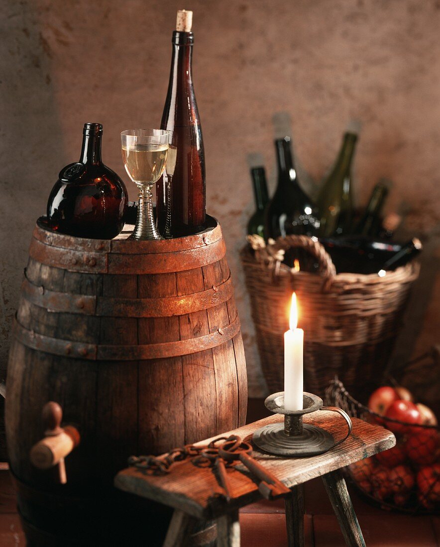Stillleben im Weinkeller mit Wein auf Fass und im Korb; Kerze