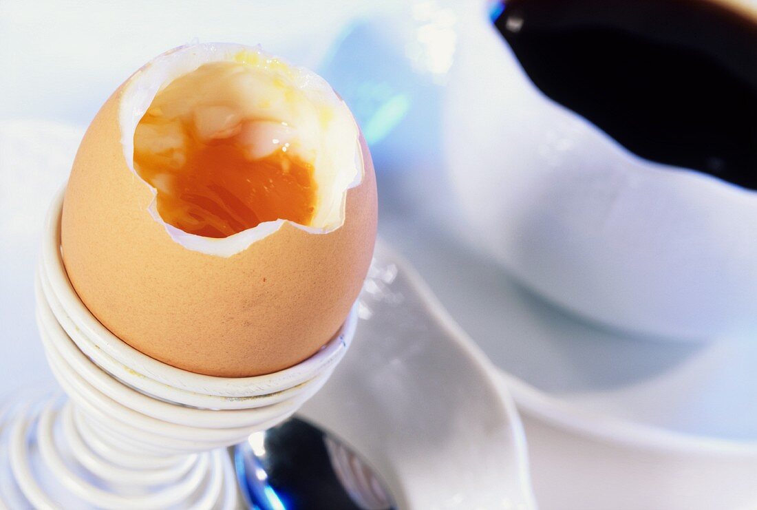Ein weichgekochtes Ei im Eierbecher neben Kaffeetasse