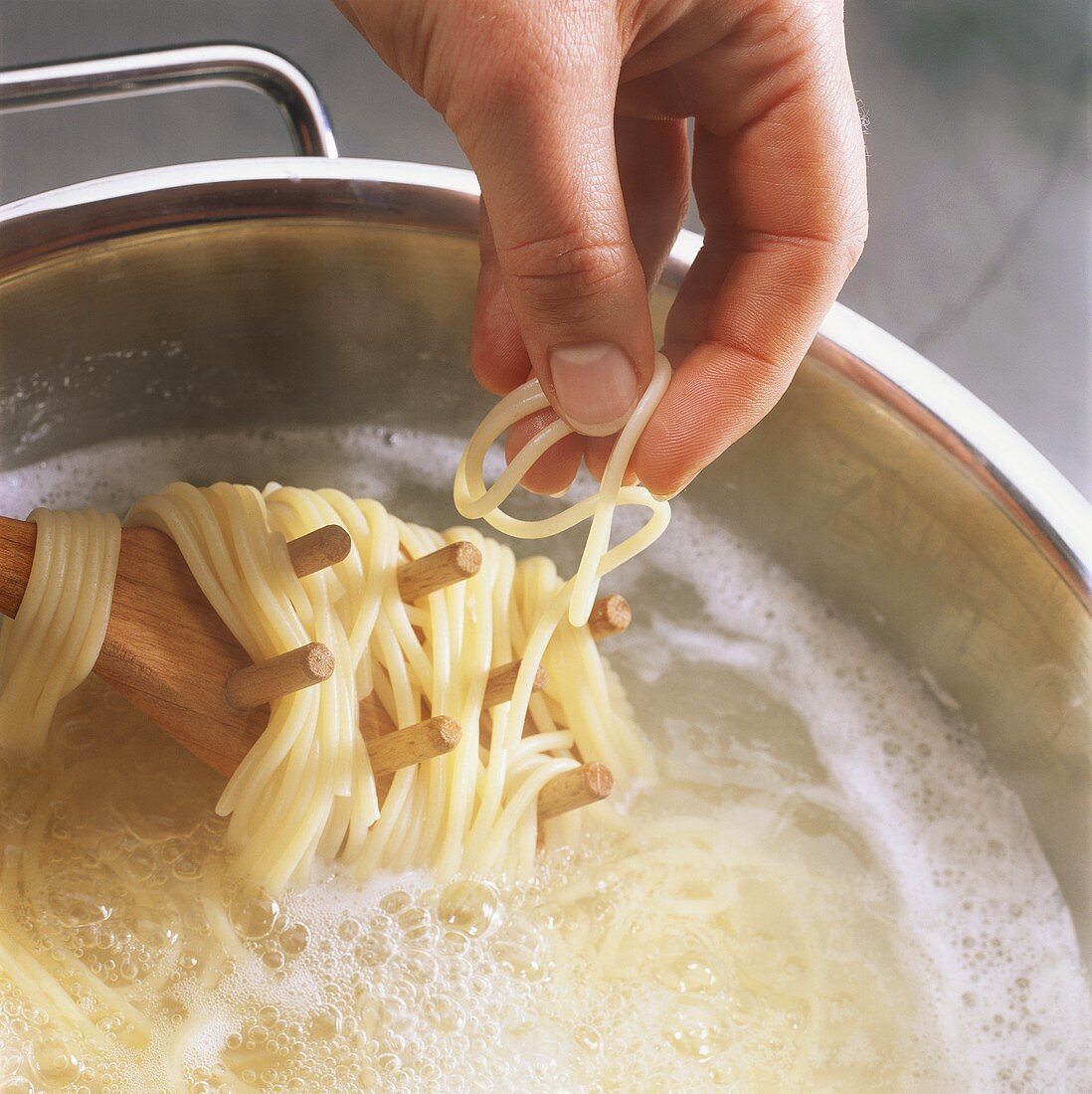 Spaghetti kochen: Hand nimmt Nudel vom Holzlöffel