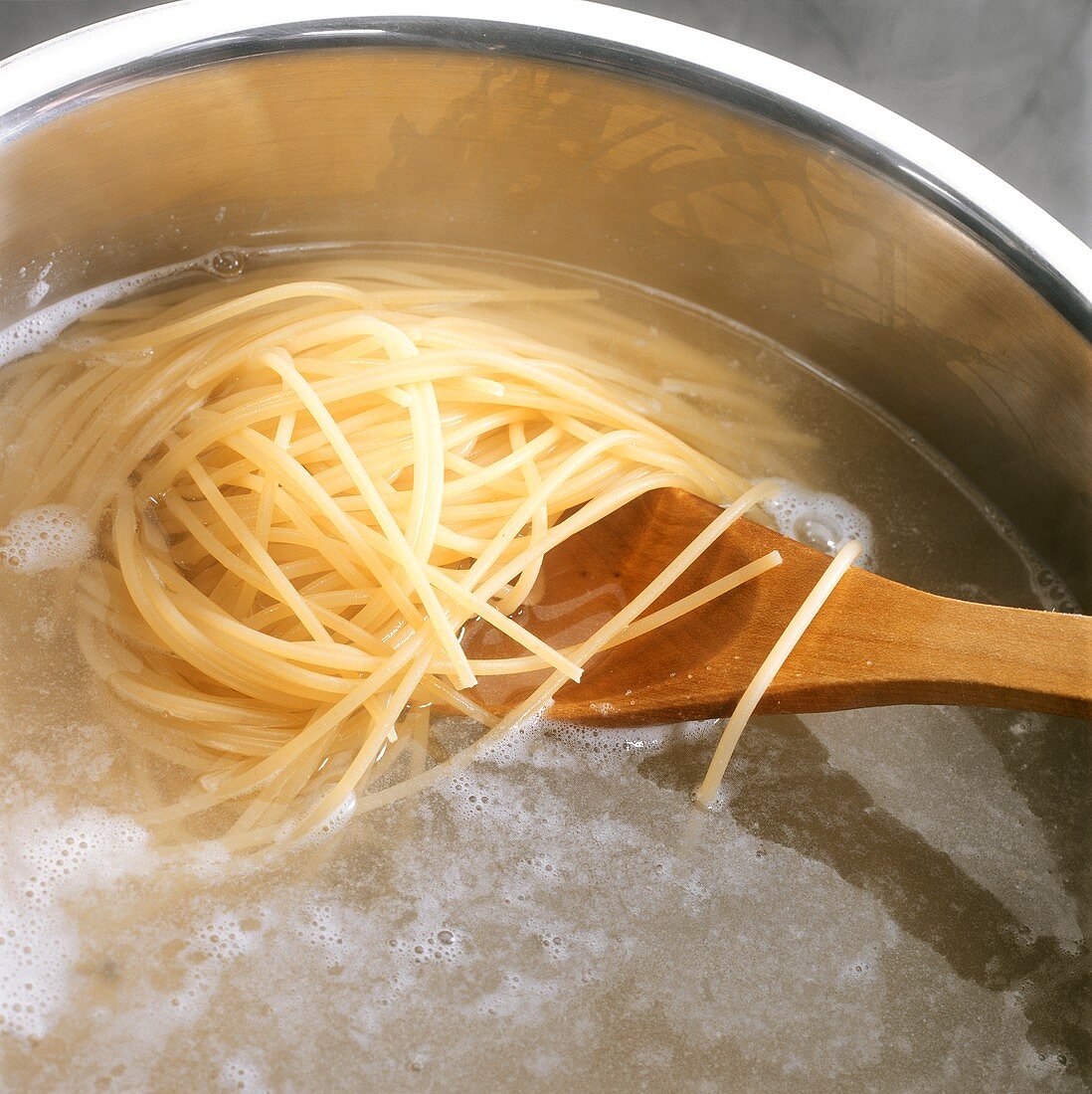 Spaghetti kochen: Nudeln mit Holzlöffel im Wasser rühren
