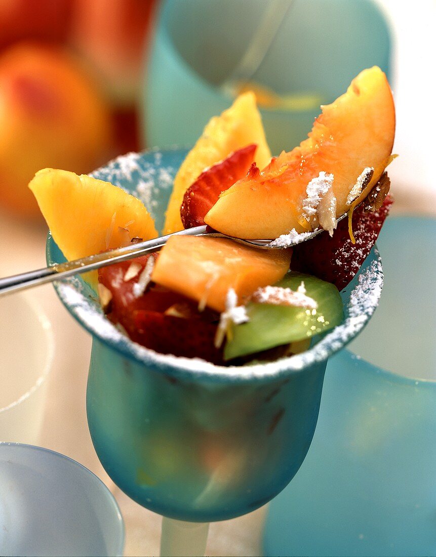 Mixed fruit salad with icing sugar in blue glass