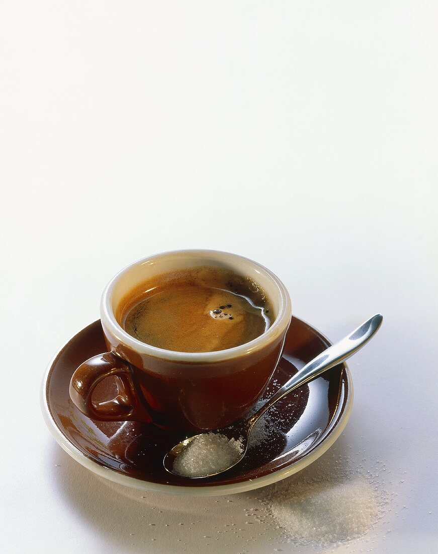Espresso in brauner Tasse; Löffel mit Zucker auf Untertasse