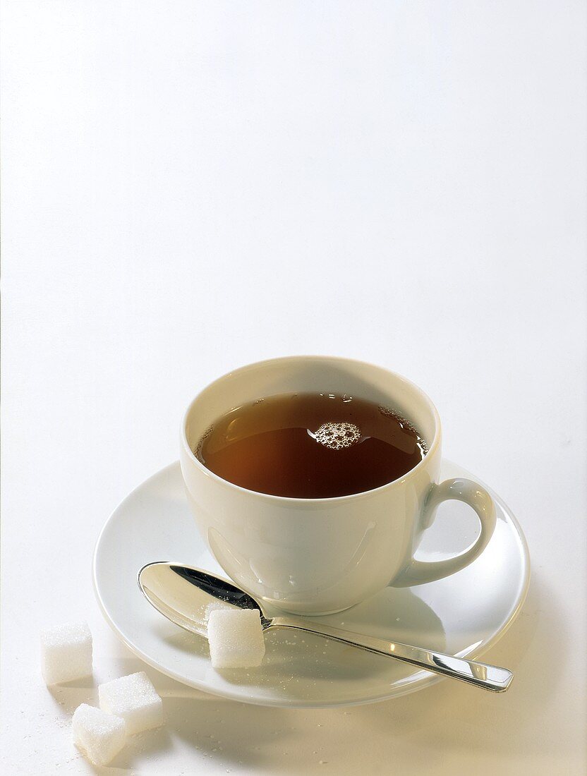 Tee in weisser Tasse; Zuckerwürfel auf Löffel und neben Tasse