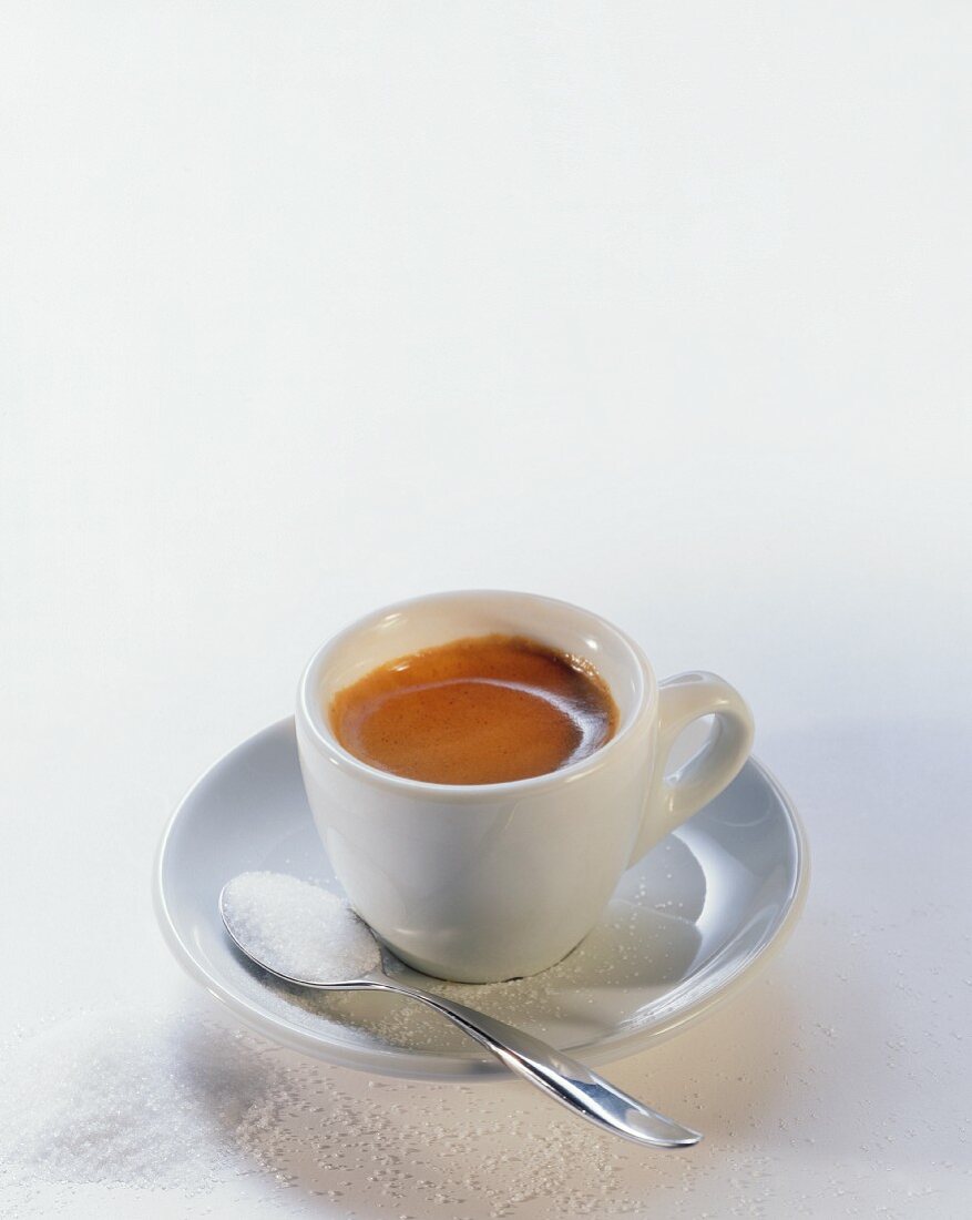 Espresso in weisser Tasse; Zucker auf Löffel und neben Tasse