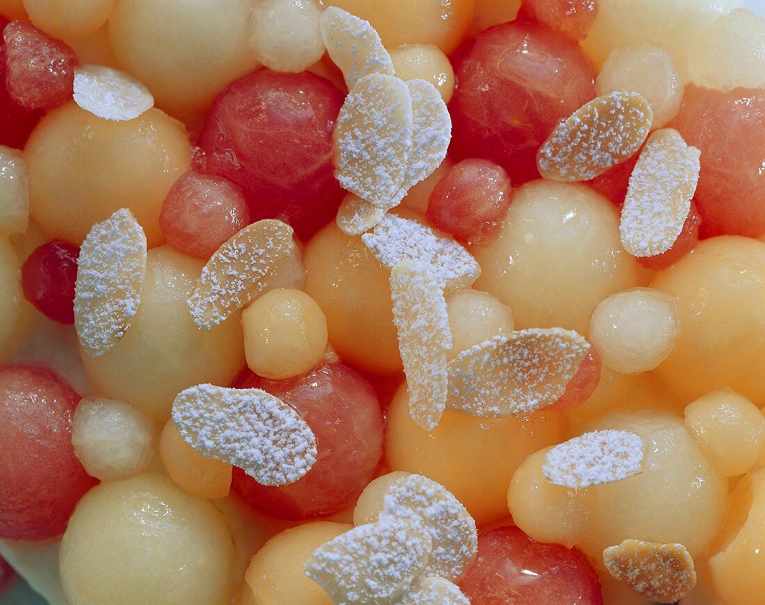 Mandelblättchen mit Puderzucker auf bunten Melonenkugeln