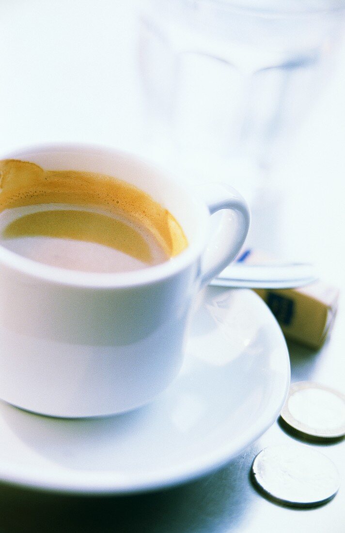 Espresso in white cup; coins, sugar lumps, glass