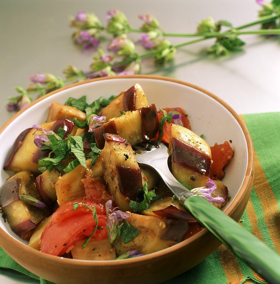 Aubergines with sage and tomatoes in a bowl with fork