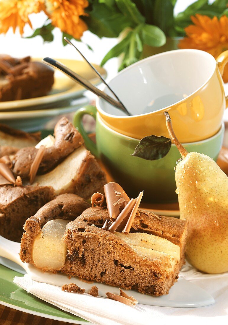 Schoko-Birnenkuchen auf Teller; frische Birne, Kaffeetassen