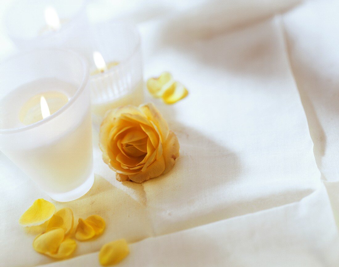 Brennende Kerzen und gelbe Rose auf weißem Tischtuch