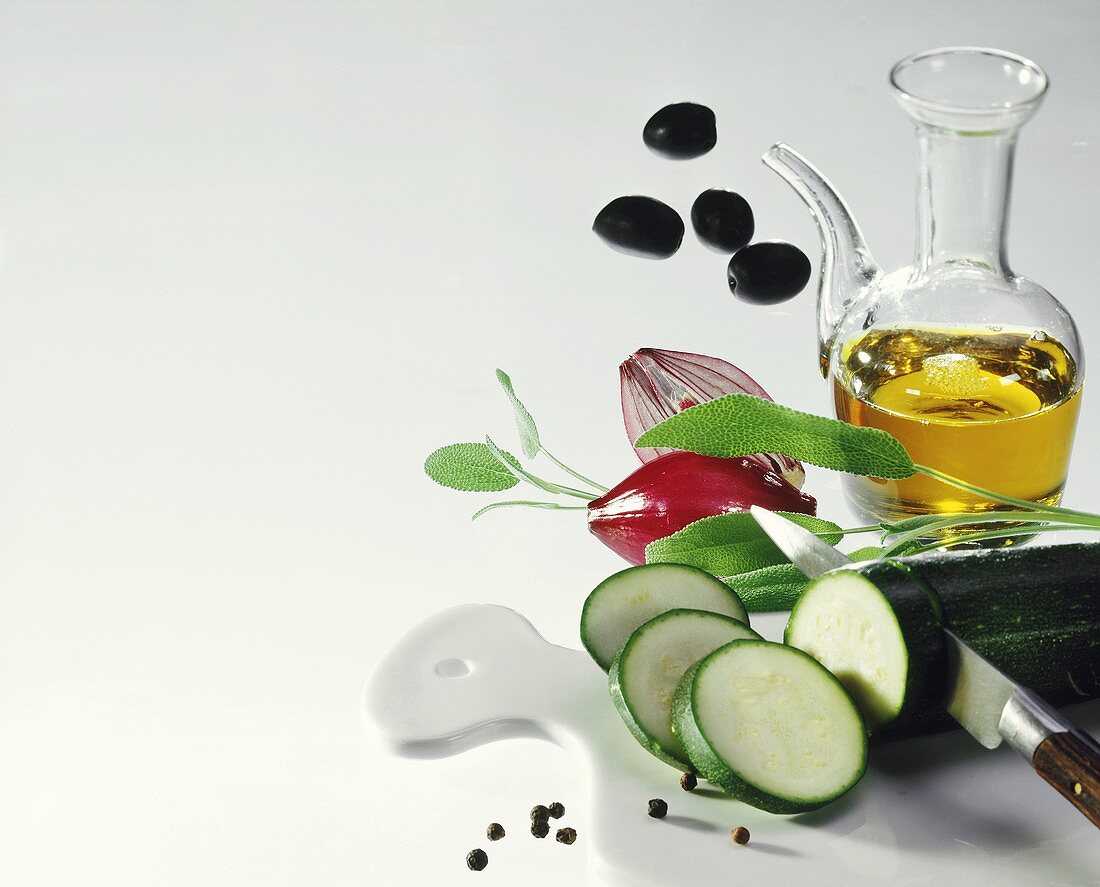 Olivenöl im Kännchen, Zucchini, Salbei, Zwiebeln und Oliven