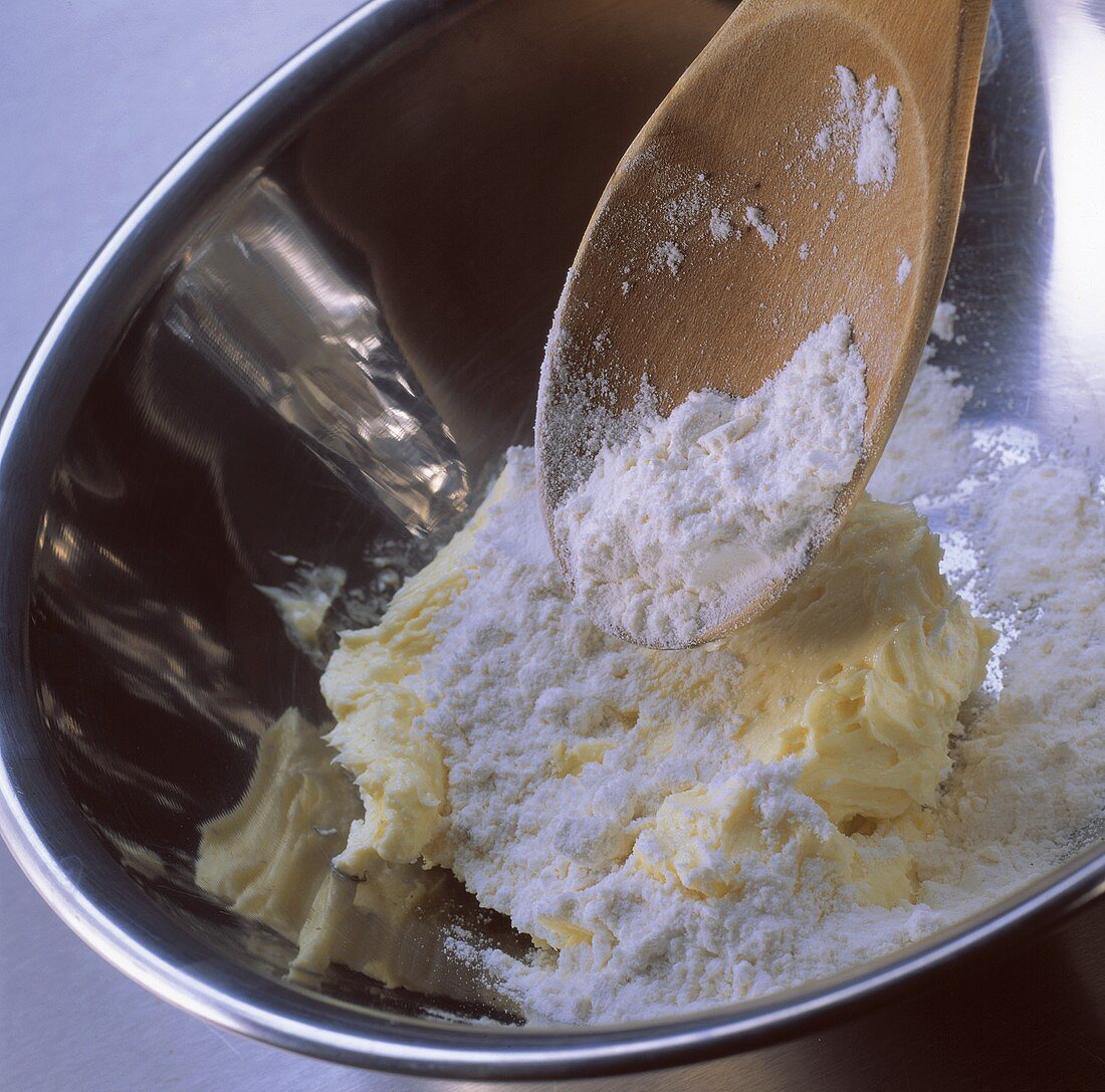 Mixing creamed cake mixture: adding flour with kitchen spoon