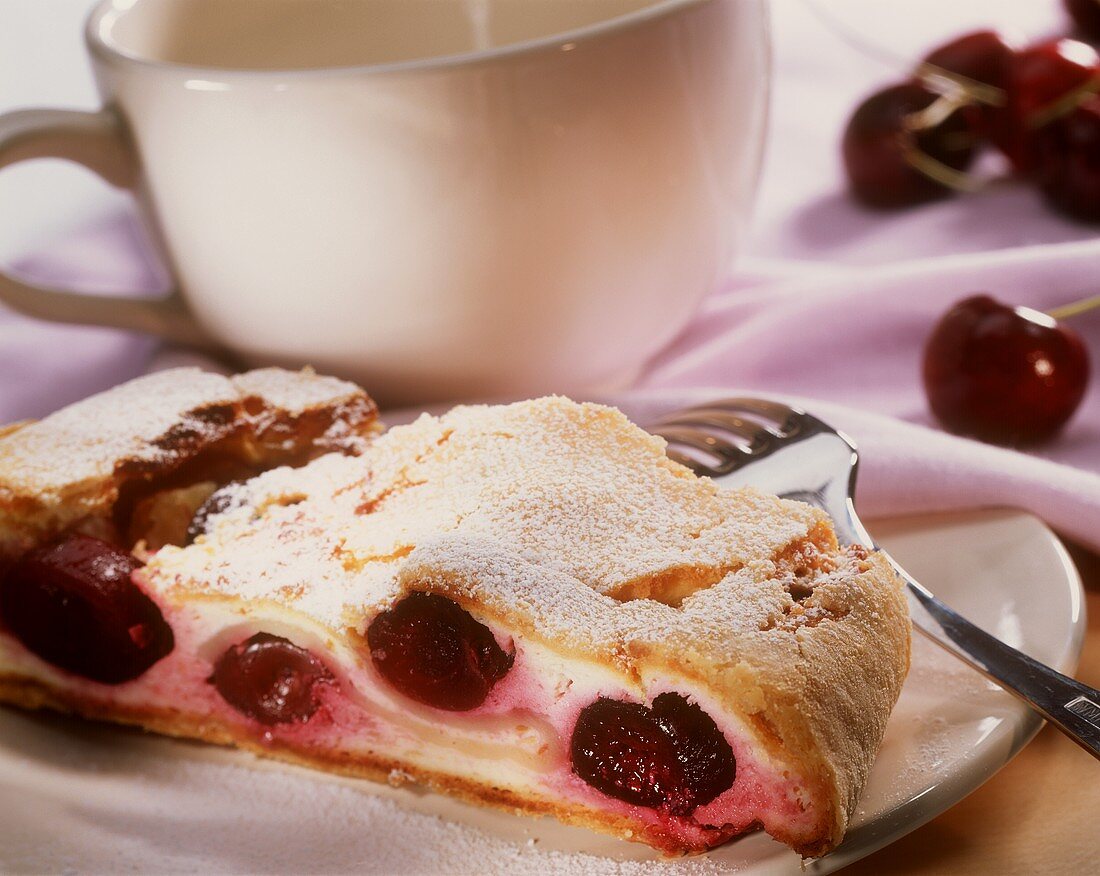 A piece of quark cherry strudel on a plate with a coffee cup