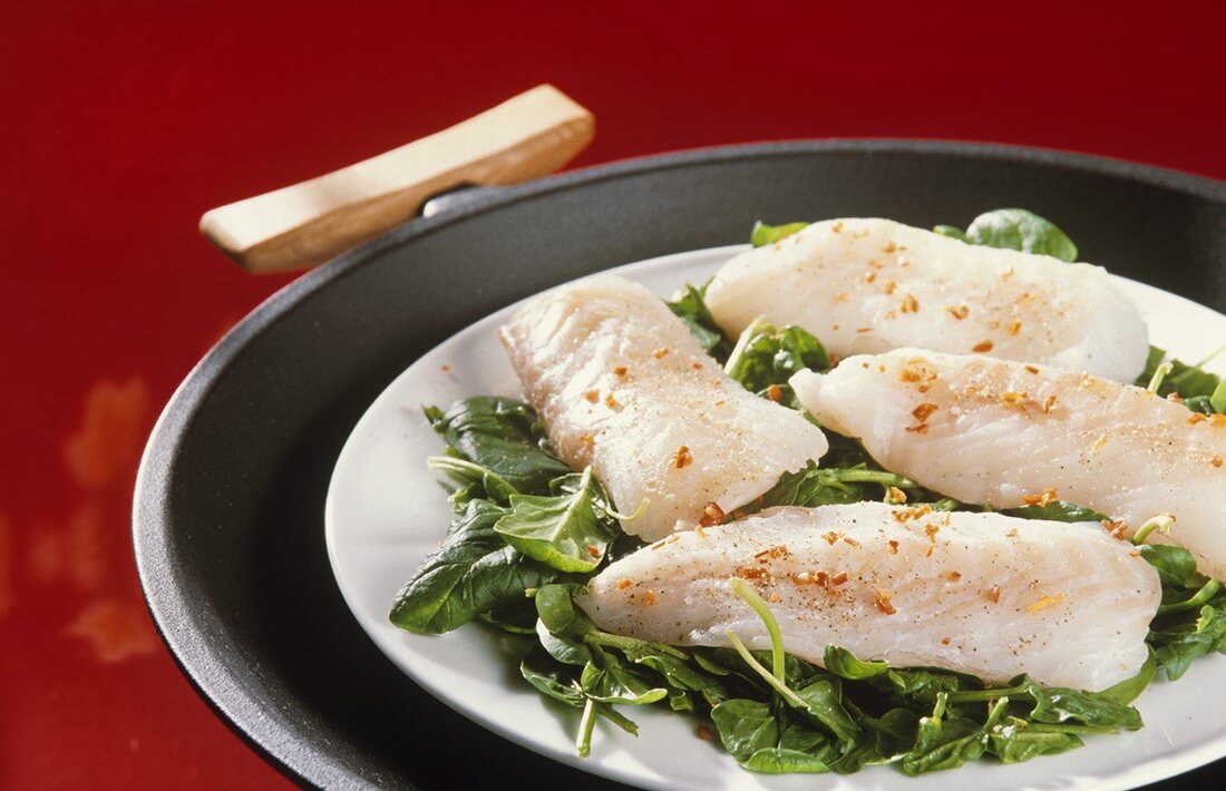 Steaming fish with spinach on plate in wok