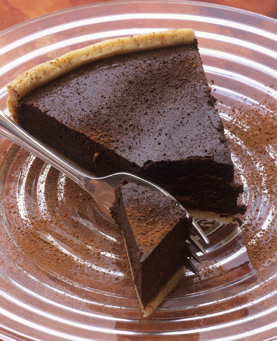 A piece of chocolate tart with cocoa powder on glass plate
