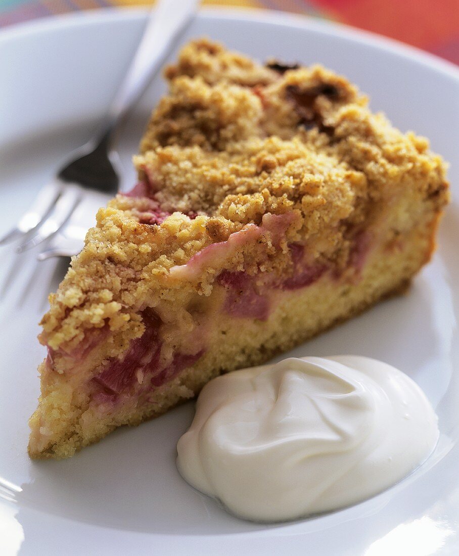 A piece of rhubarb cake with cream on plate with fork