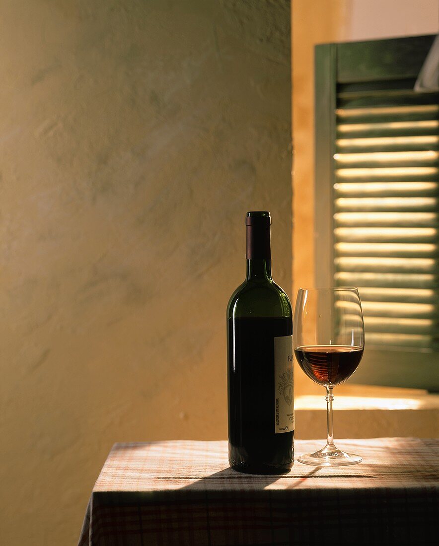 Rotwein in Flasche und Glas auf Tisch vor einem Fenster