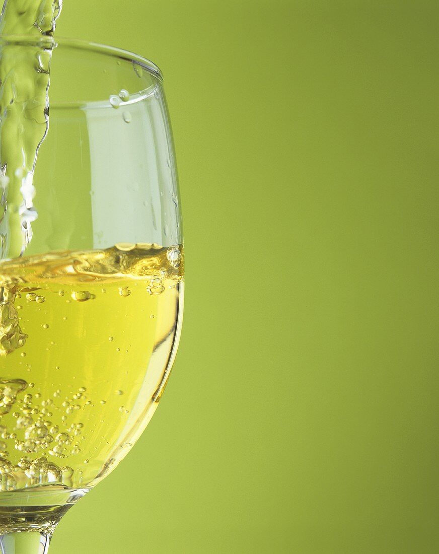 Pouring white wine into a glass against a green background