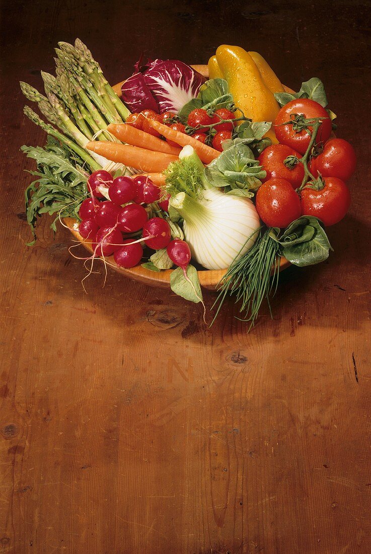 Fresh vegetables in a wooden bowl, including fennel, radishes