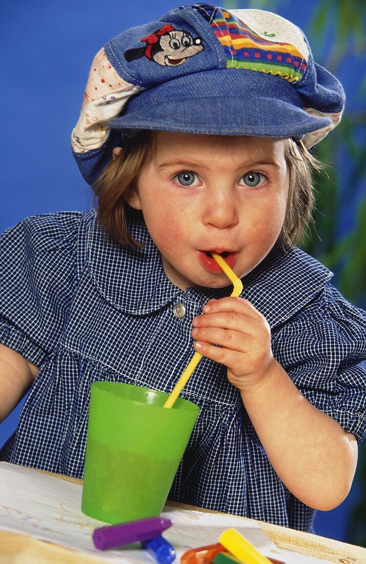 Small girl drinking juice from beaker through a straw