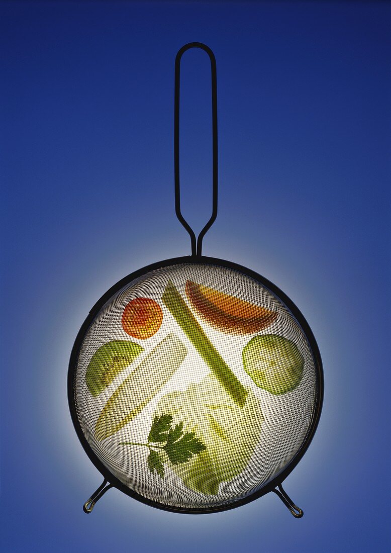 Vegetables, salad leaves & fruit slices under a strainer