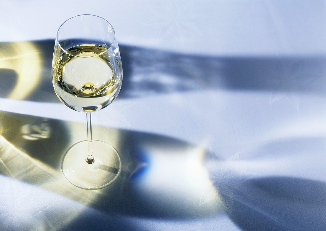 A glass of white wine with shadows on a white table cloth