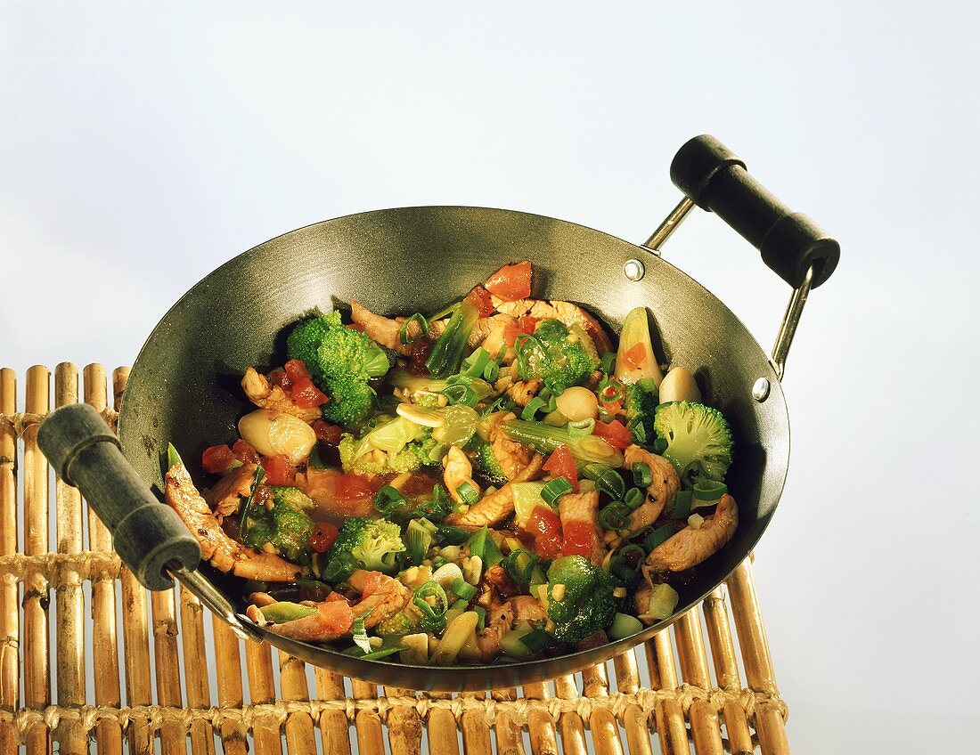 Strips of turkey with vegetables in wok on bamboo tray