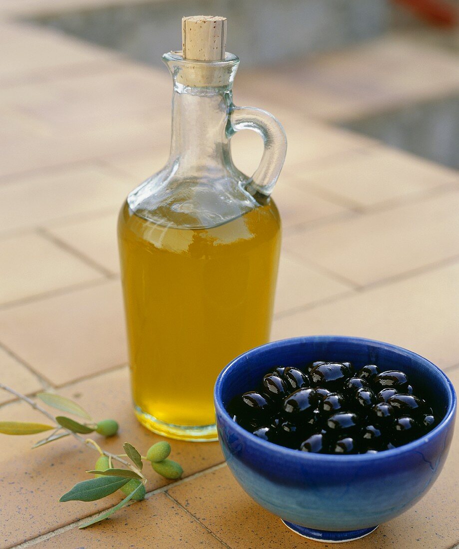 Olivenöl und eine Schale schwarze Oliven