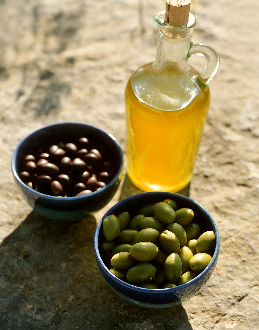 Olive oil and two bowls of black and green olives