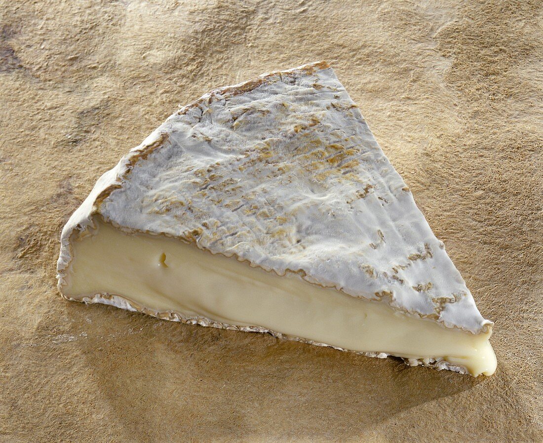 Ein Stück Brie de Melun auf braunem Untergrund