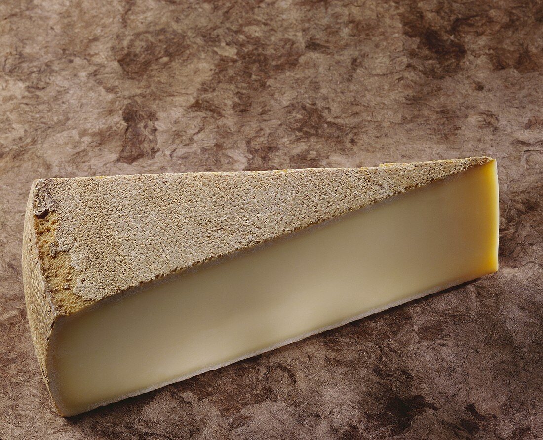 A piece of Gruyere on brown background