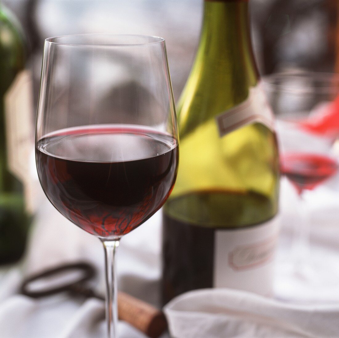 Rotweinglas vor einer halbvollen Flasche Rotwein auf Tisch