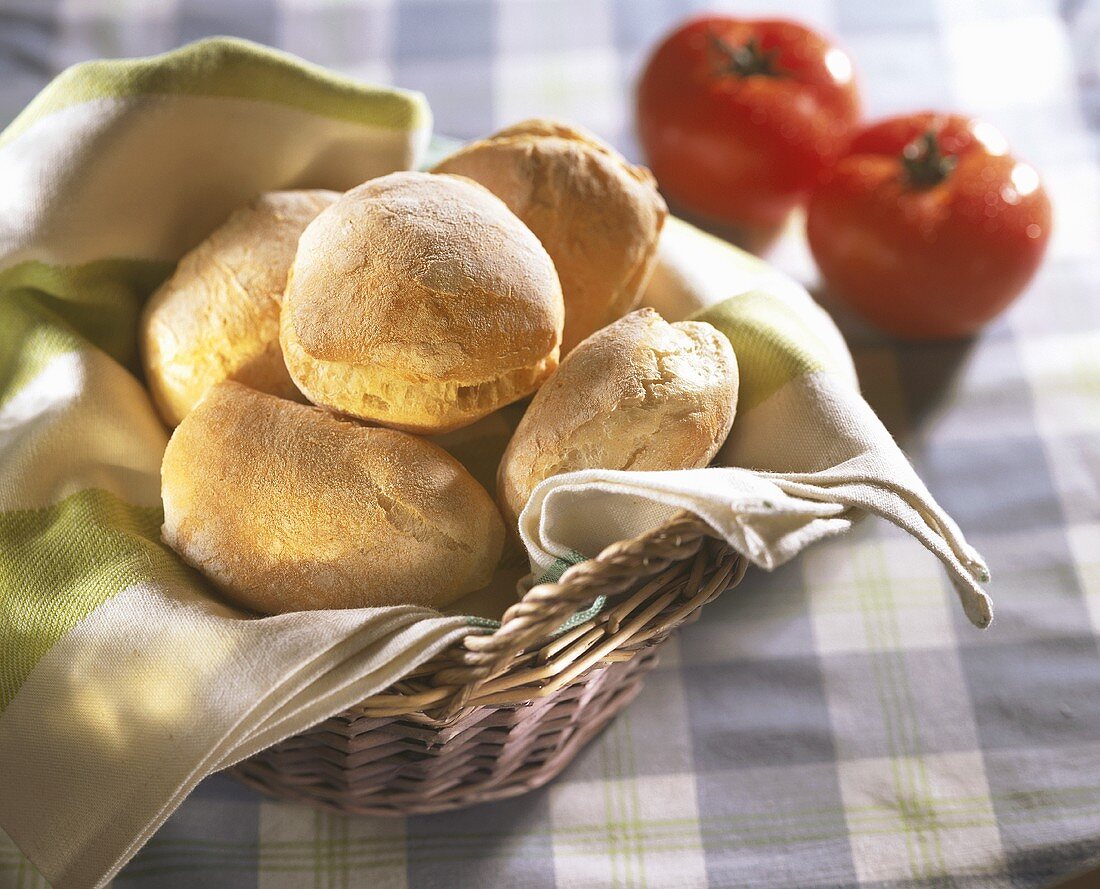 Brötchen im Brotkorb, dahinter zwei Tomaten