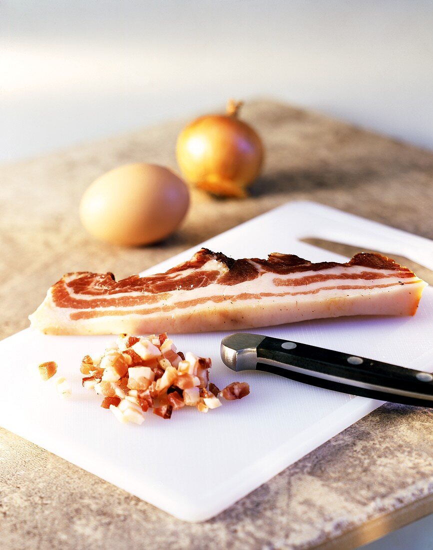 Bacon slice and cube with a knife on a chopping board