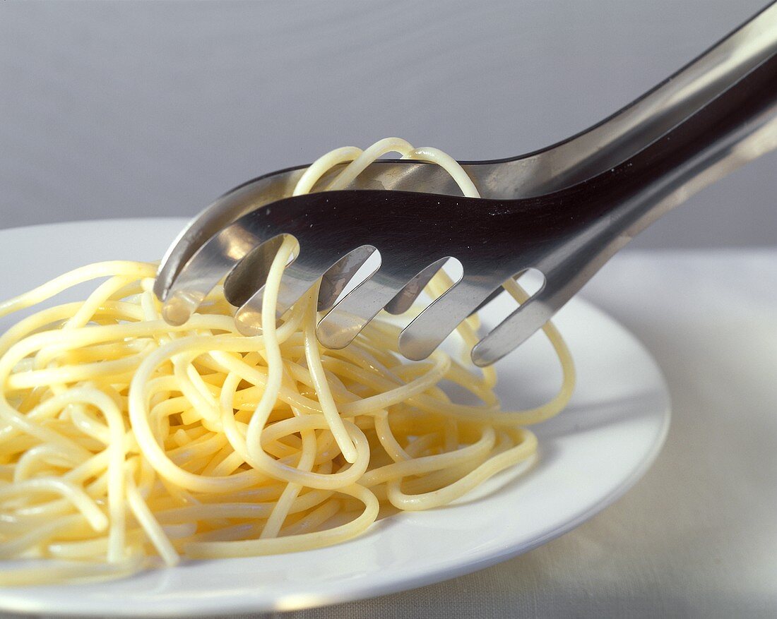 Cooked spaghetti with spaghetti tongs on white plate