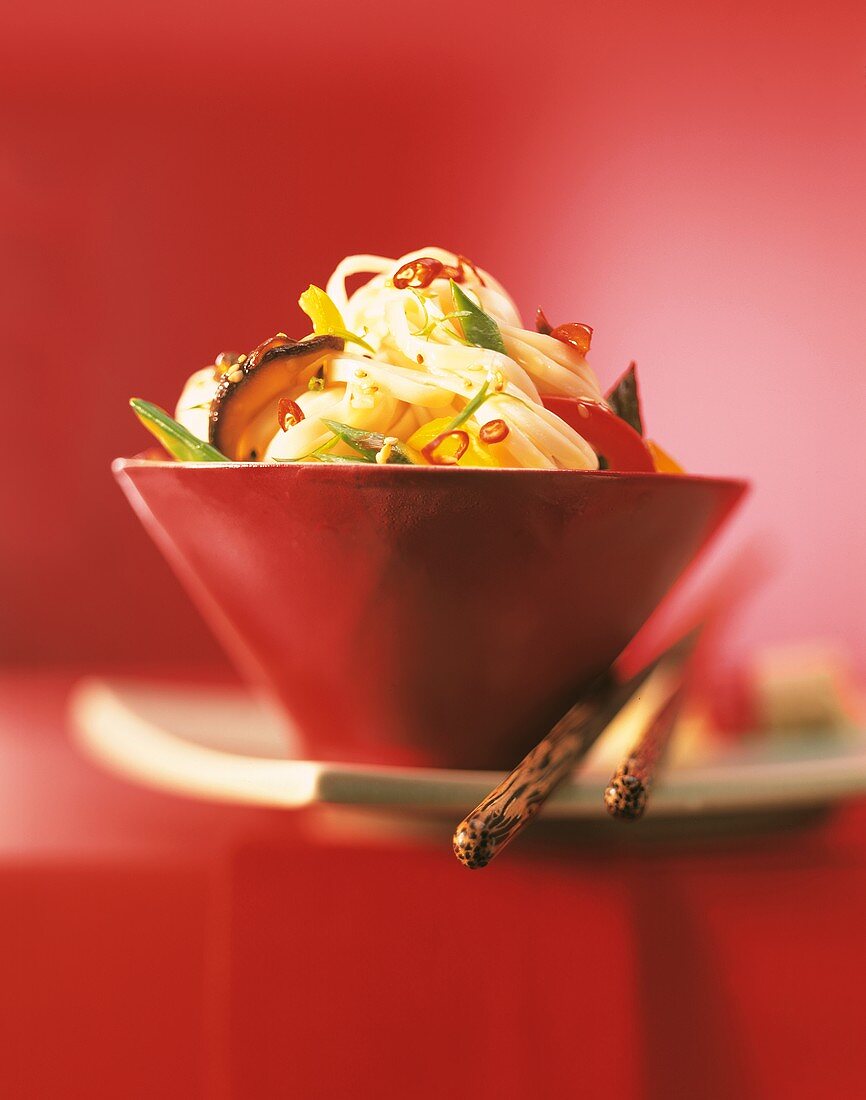 Asian noodles with vegetables in a red bowl