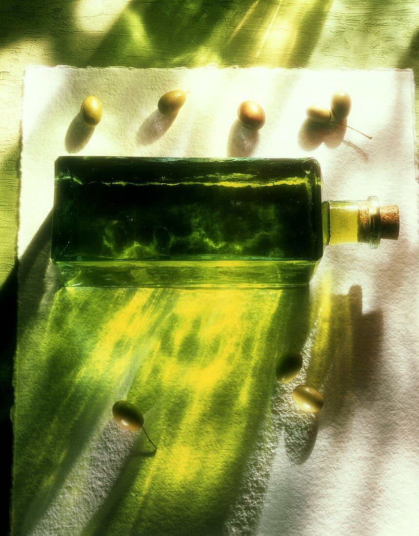 A bottle of olive oil and fresh green olives