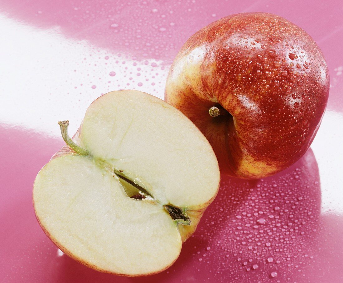 Ganzer und halber Jonagold Apfel auf rosa Untergrund