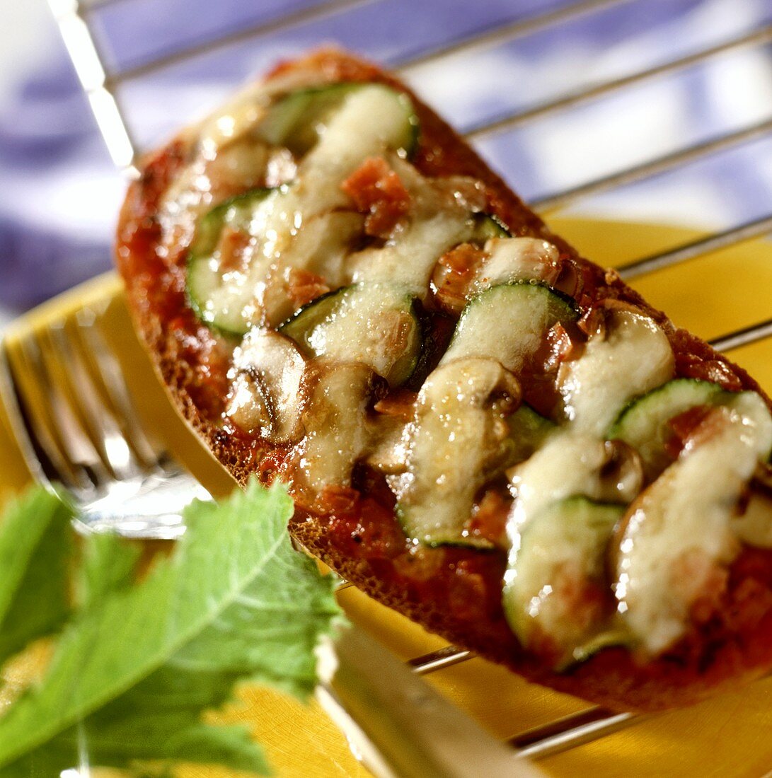 Kleine Brotpizzen mit Tomaten und Zucchini auf Kuchengitter