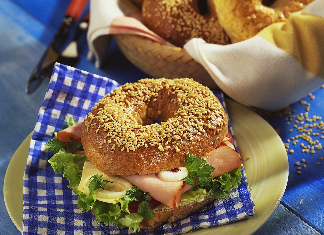 Sesam-Bagel mit Schinken und Käse vor Brotkorb