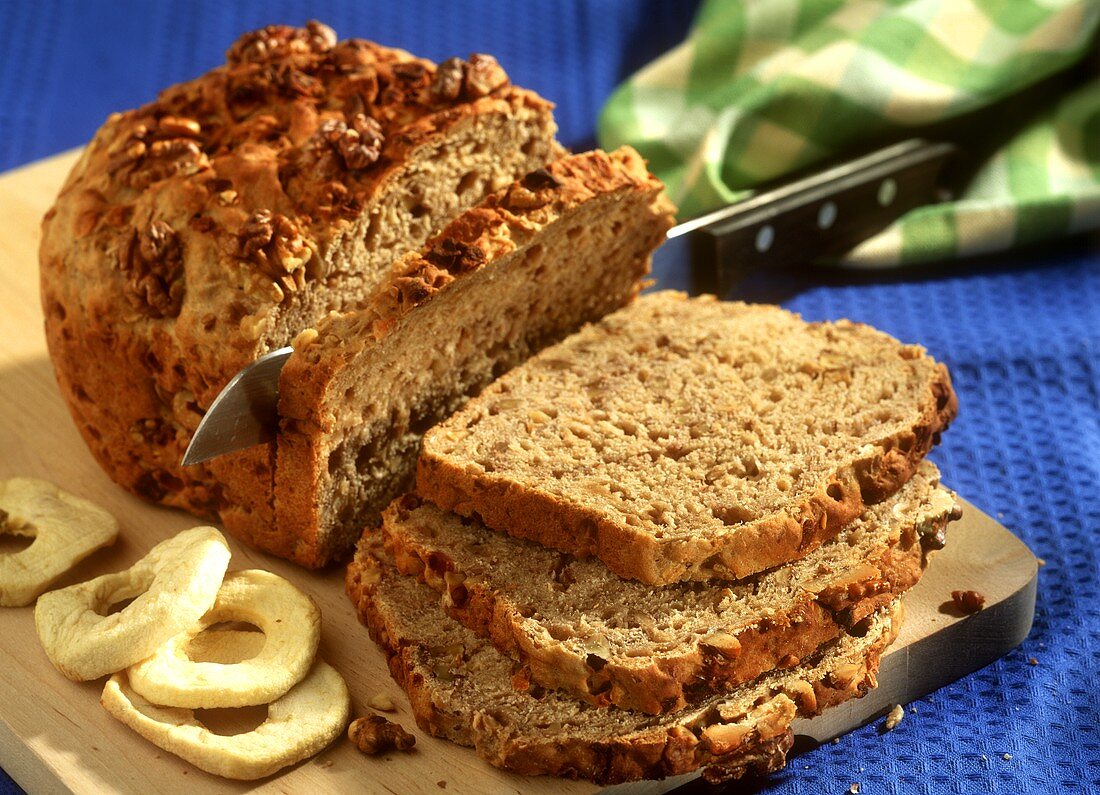 Apple and walnut bread, partly sliced on chopping board