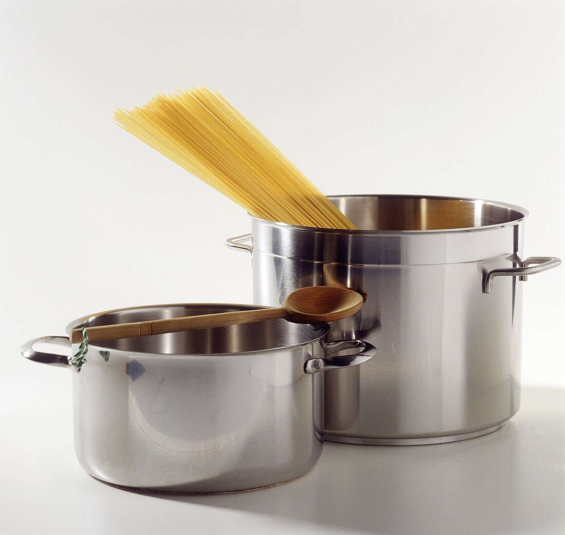 Two pans with wooden spoon and spaghetti