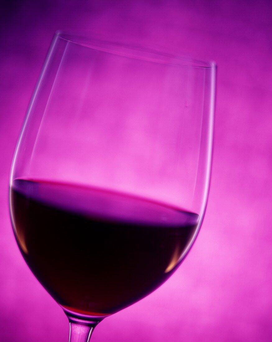 Halb gefülltes Rotweinglas vor violettem Hintergrund