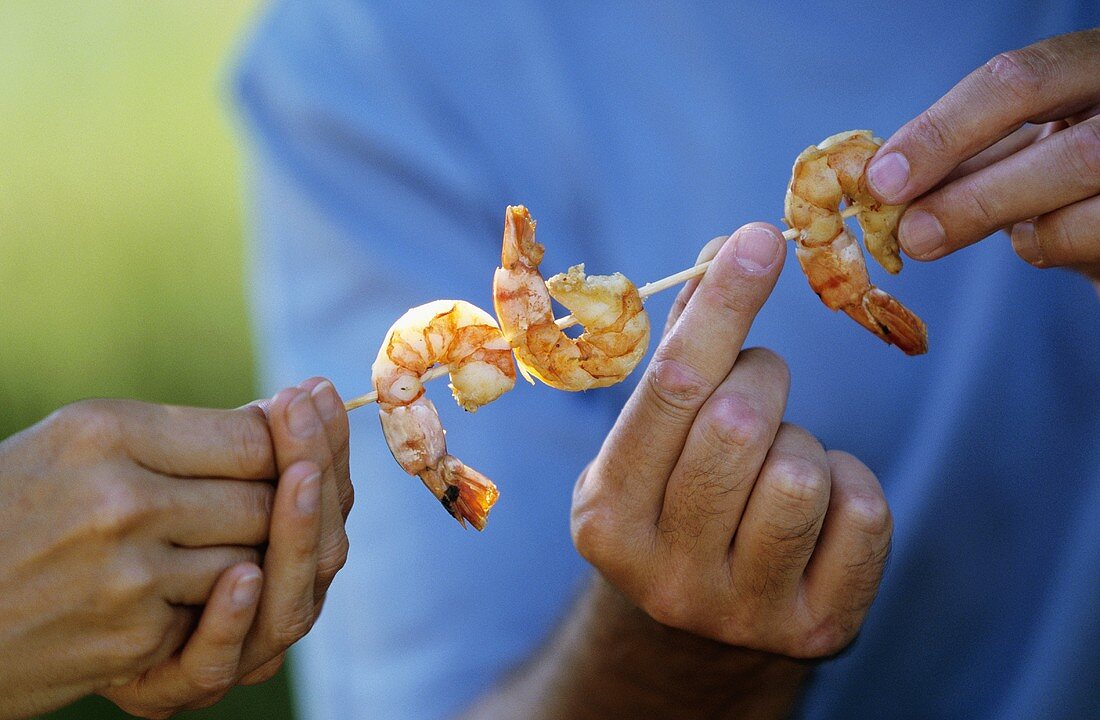 Hands holding shrimp kebab