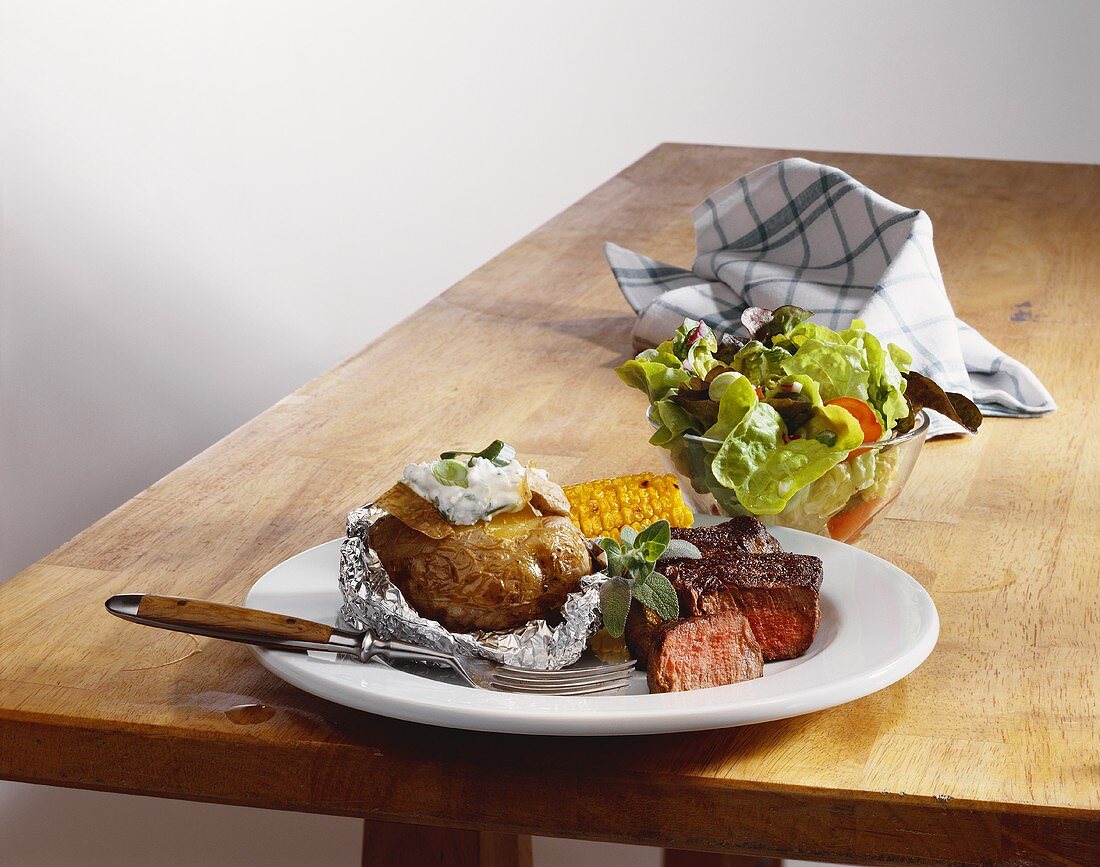 Beef fillet with baked potato, corncob and salad