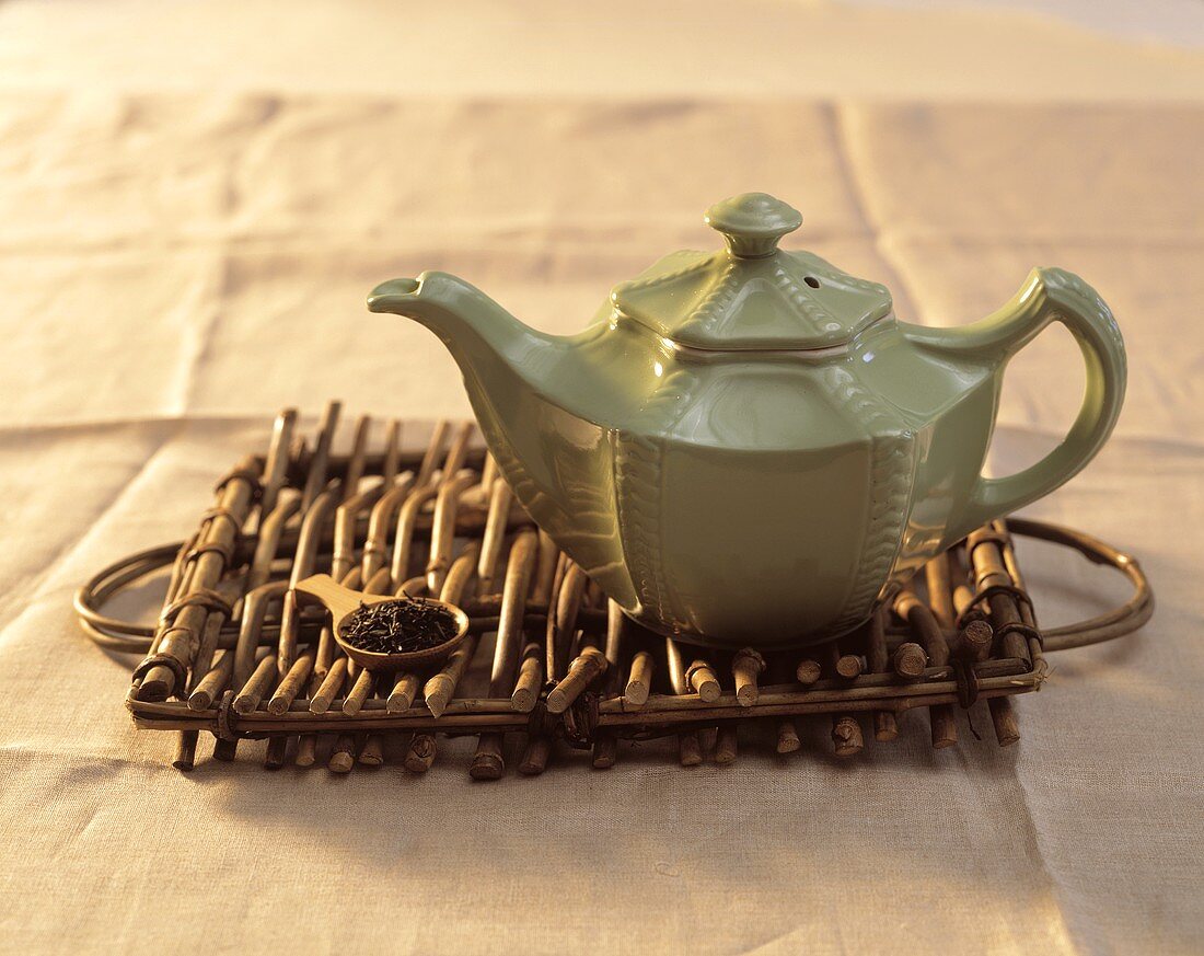 Grüne Teekanne auf Holztablett mit einem Löffel Teeblätter