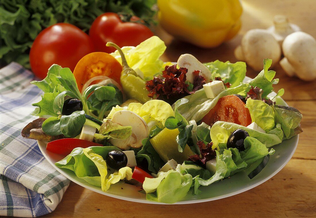Mixed salad leaves on plate, vegetables behind